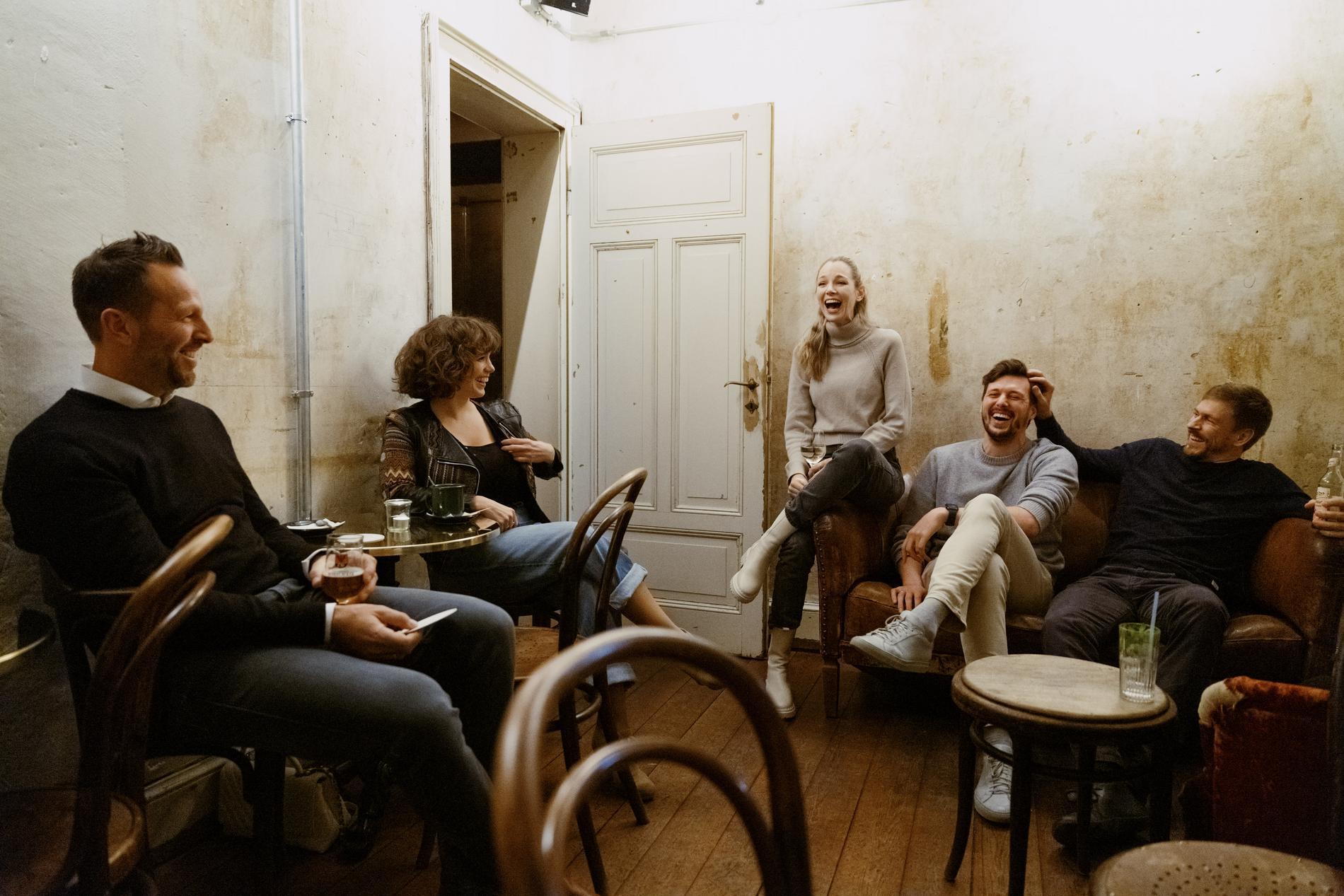 Fünf Personen sitzen in einer Bar zusammen und lachen während sie Getränke genießen.