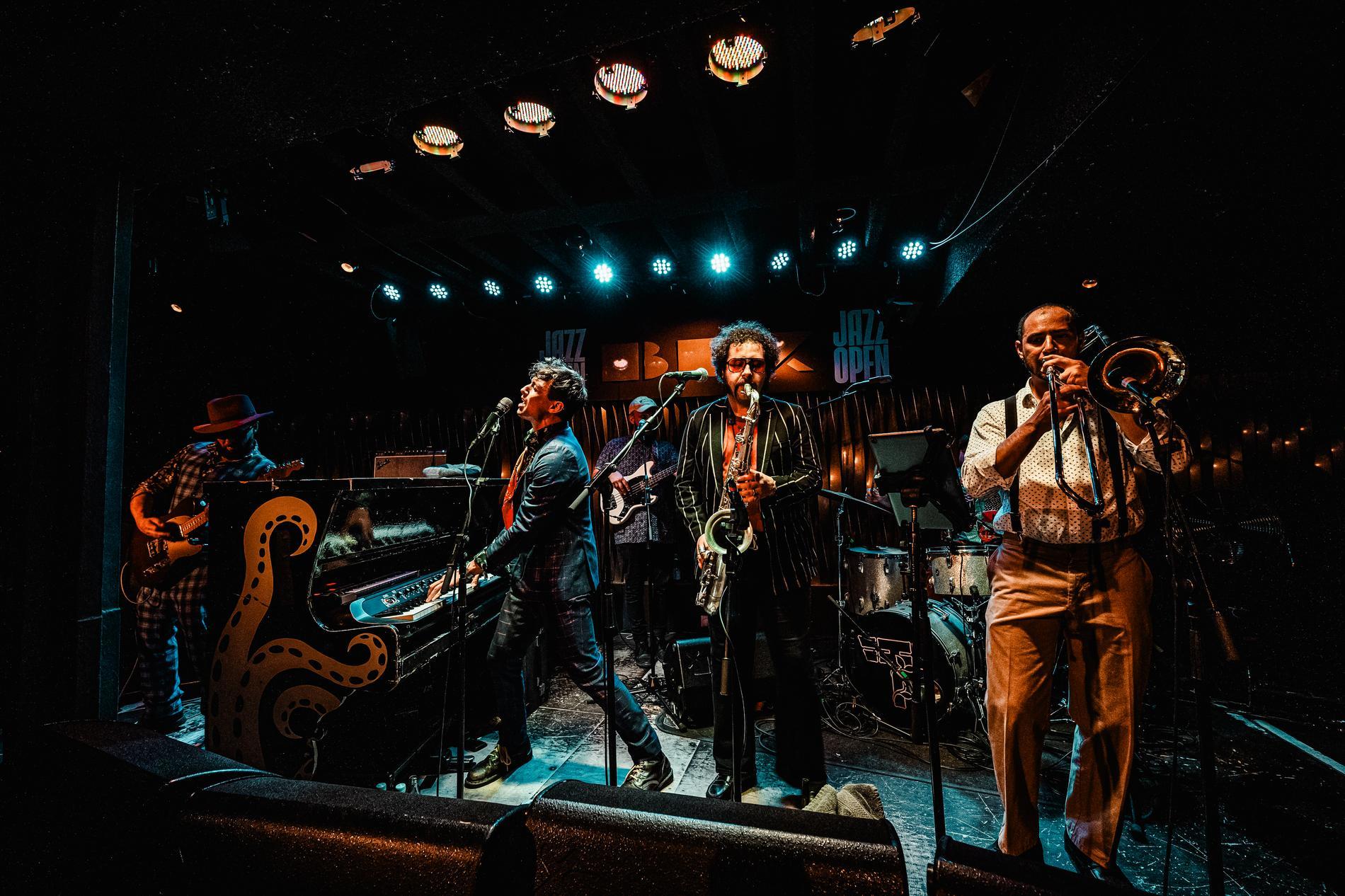 Drei Männer spielen Klavier, Saxophon und Trompete auf einer Bühne.
